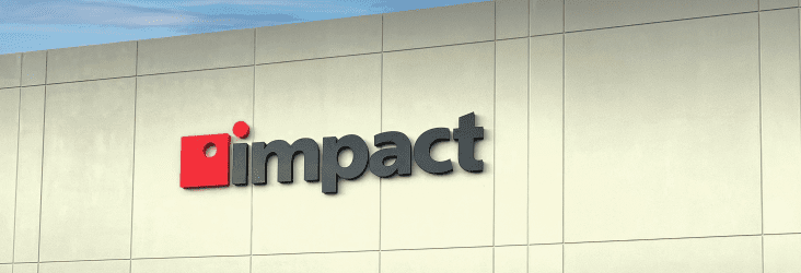 Empty parking lot leading to large white building with Impact logo center top.