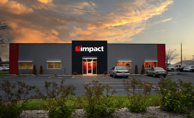 Impact Networking logo on a black and white office building at sunset with green shrubbery in the foreground