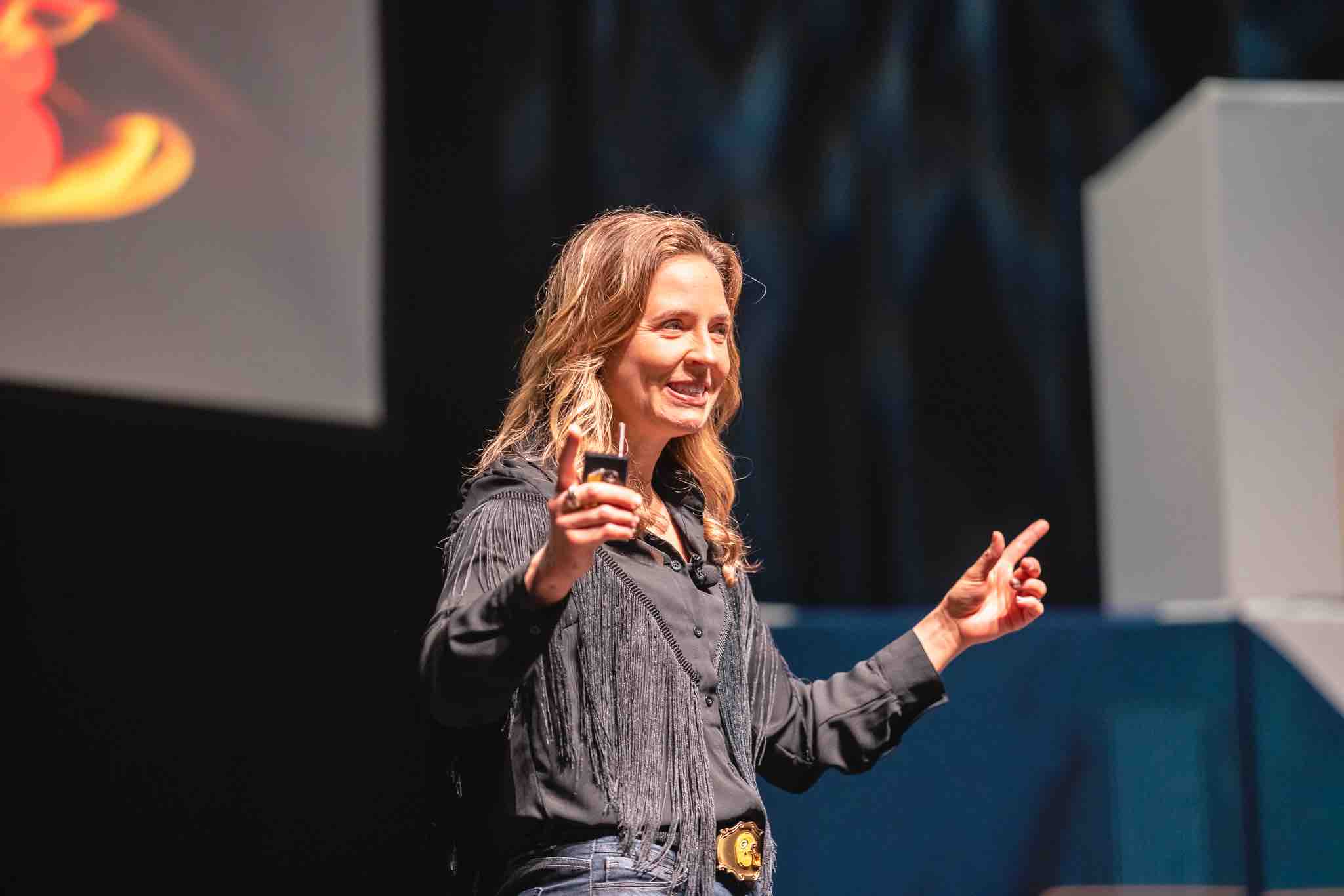 woman on stage smiling holding her arms and pointing