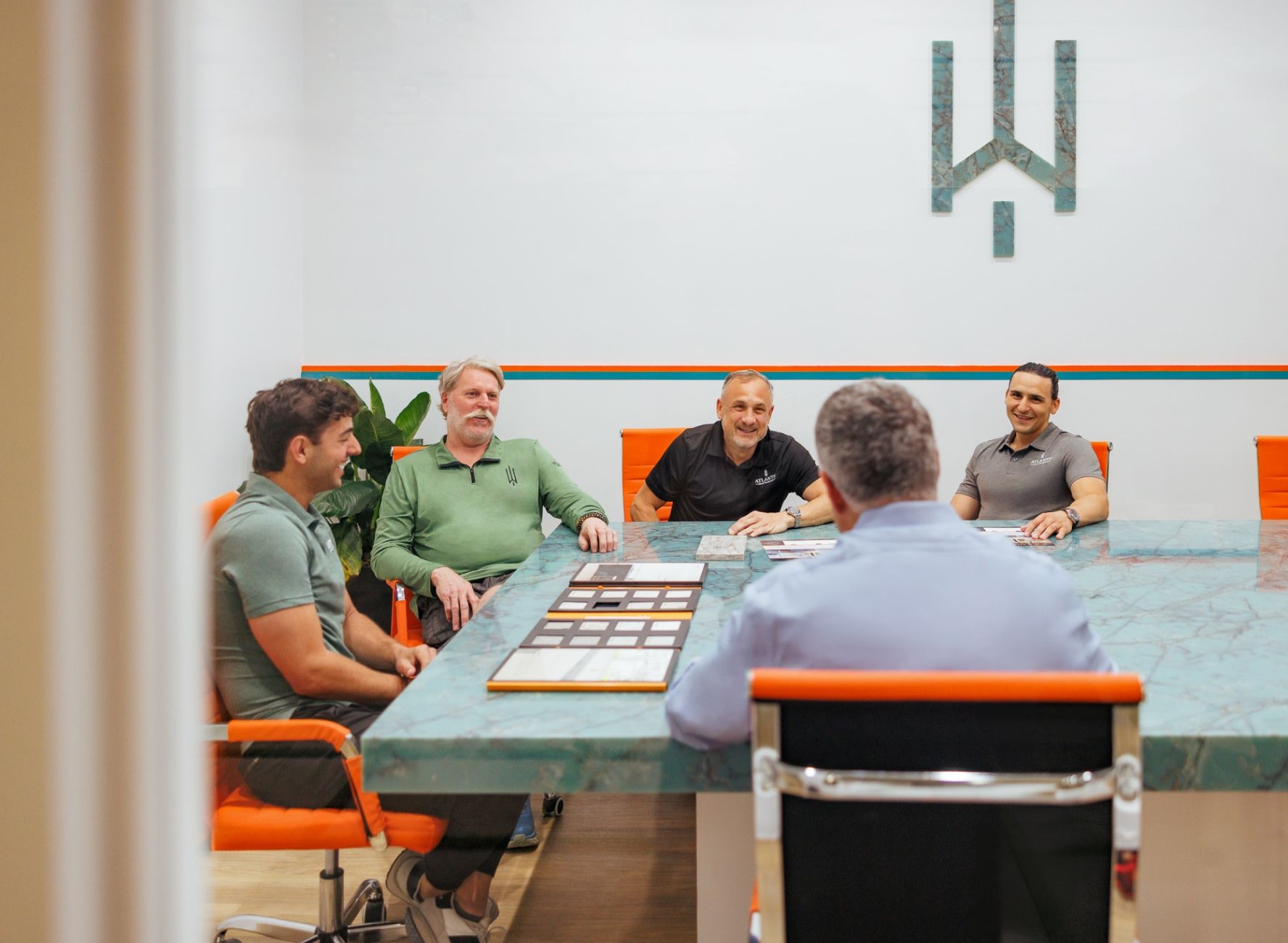 Atlantis Owners meeting with prospective client in conference room with custom green marble table, orange chairs, and atlantis logo on the wall made of stone