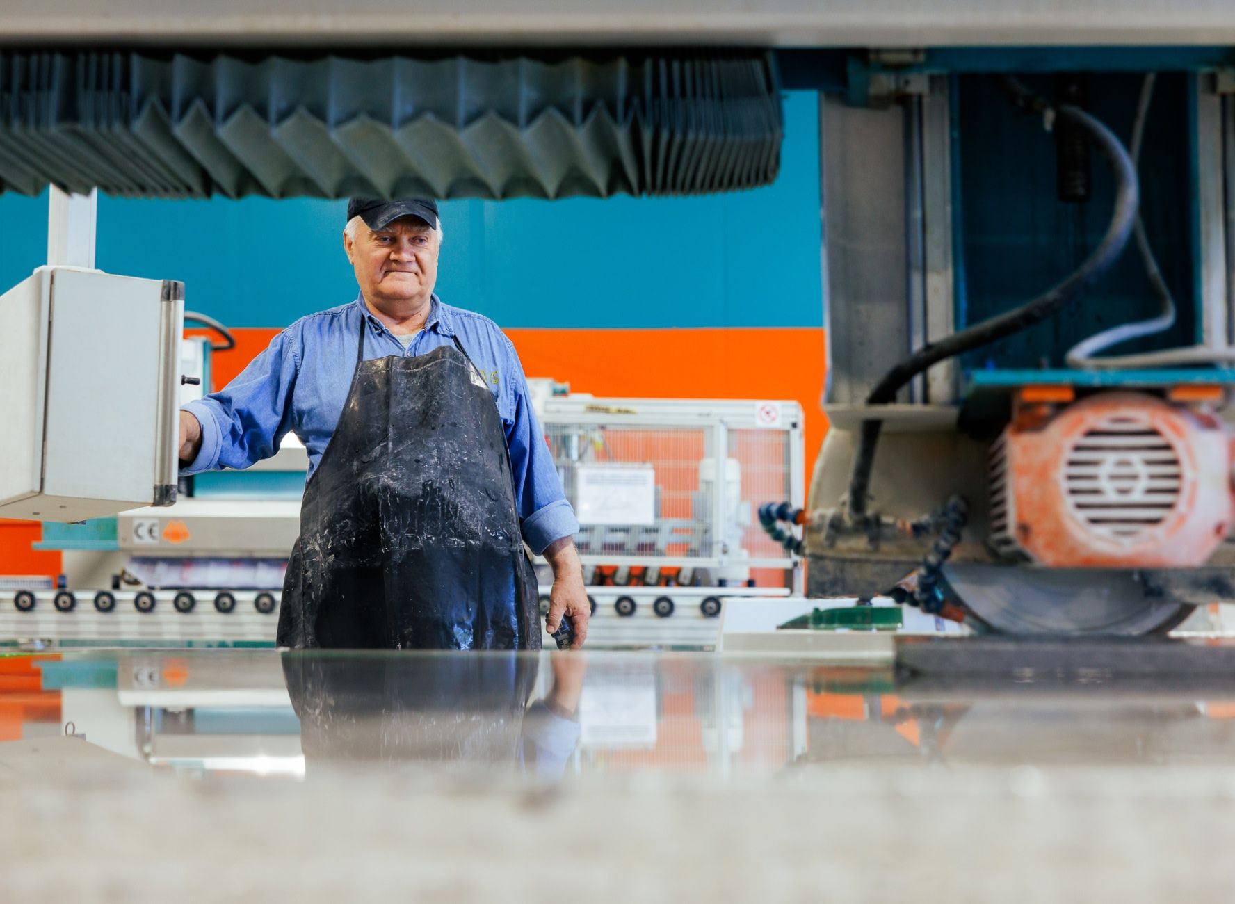Fabrication shop foreman watching Poseidon cutting machine spray water on stone slab while wearing apron