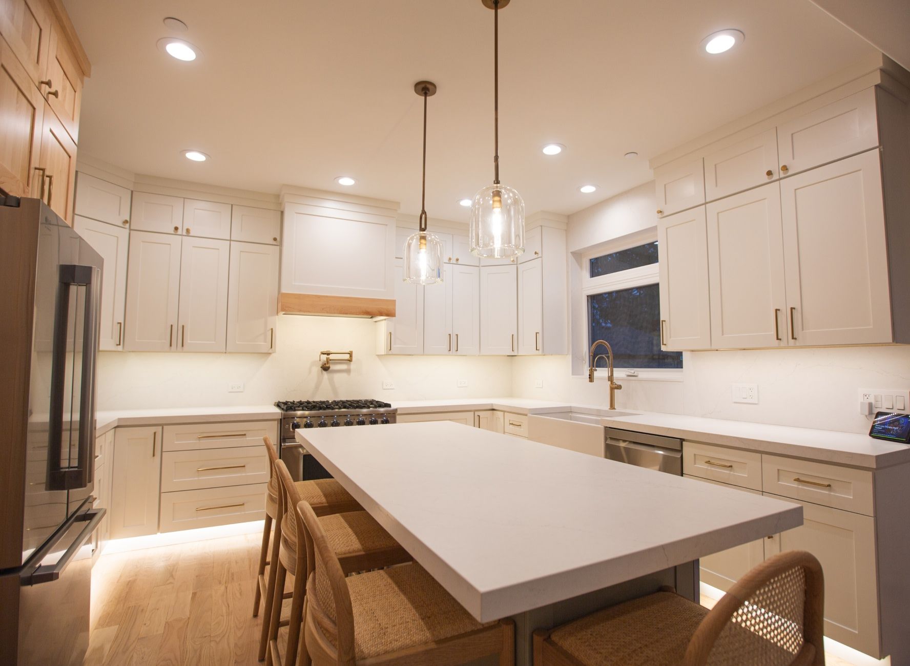 Corner kitchen has white countertops, white cabinets with gold handles, stainless steel appliances, and underlighting