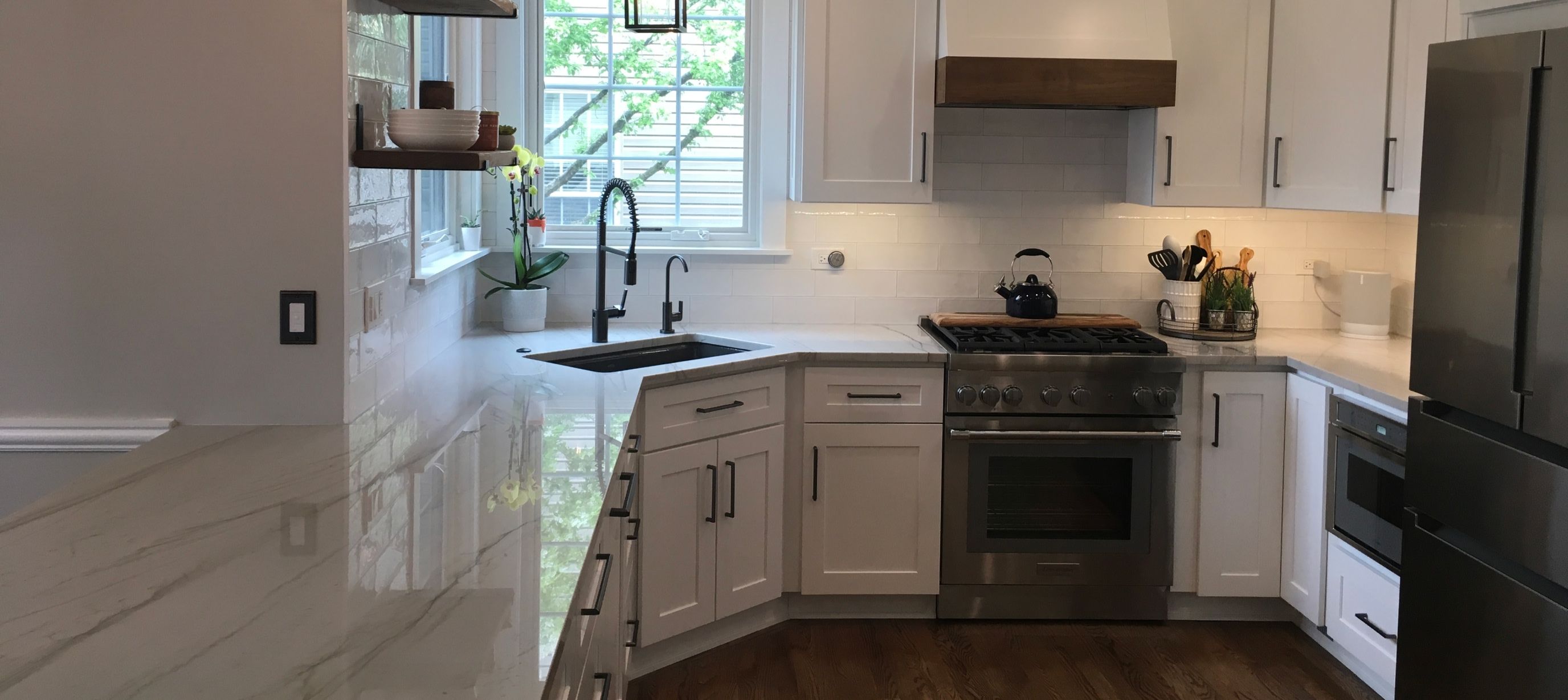 white and grey marbled countertop in corner kitchen with white cabinetry with black handles