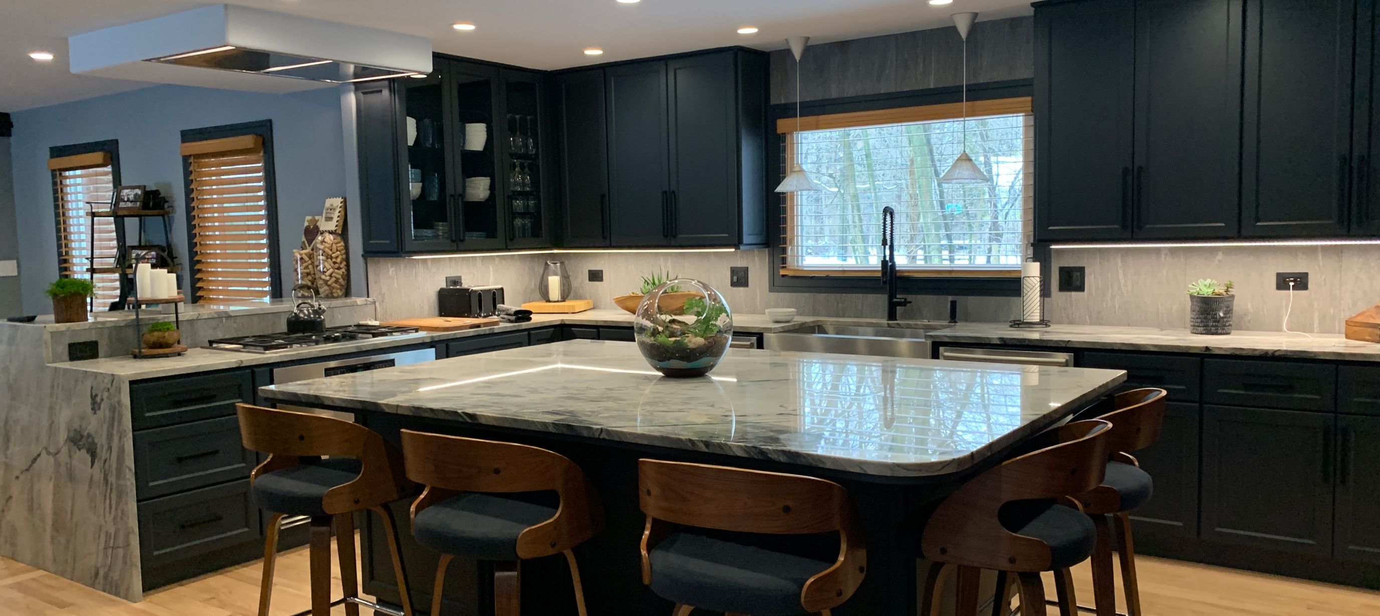 Kitchen with custom stonework countertops and island with black cabinets and wooden barstools
