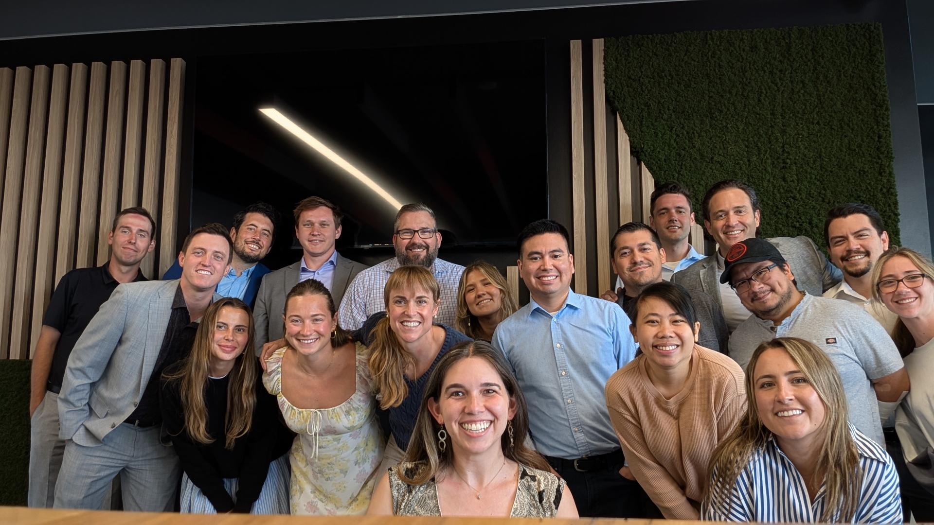 A group of colleagues taking a picture together in front of a wood and plant wall in their new Culver City office